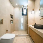 Κύριο μπάνιο με επένδυση travertine, μαύρο σκαλιστό νιπτήρα και χρυσές εντοιχισμένες μπαταρίες