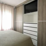 Υπνοδωμάτιο με εντοιχισμένη ντουλάπα, τηλεόραση και λευκές συρταριέρες